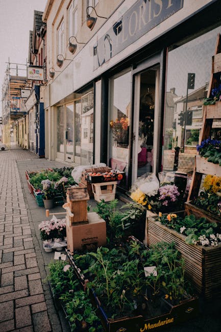 Outside the storefront of Floristenfield, a variety of fresh flowers and potted plants are displayed along the sidewalk. The arrangement includes vibrant flowers such as yellow, purple, and white blos